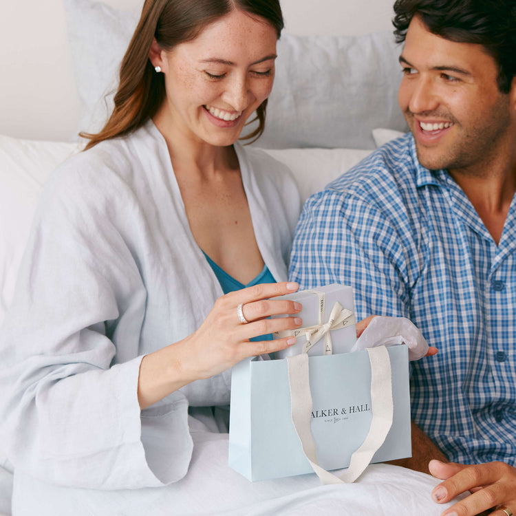 Couple sitting together on a bed, woman opening a Walker & Hall box