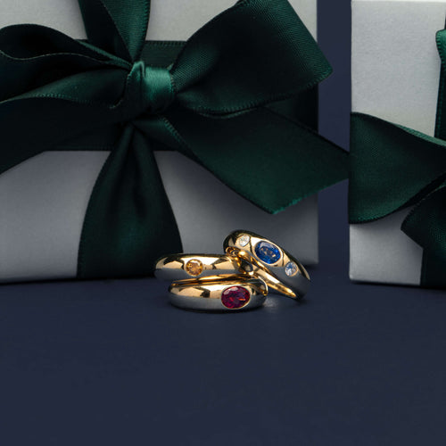 Coloured gemstone Kylie Rings on navy background with wrapped Walker & Hall gift boxes