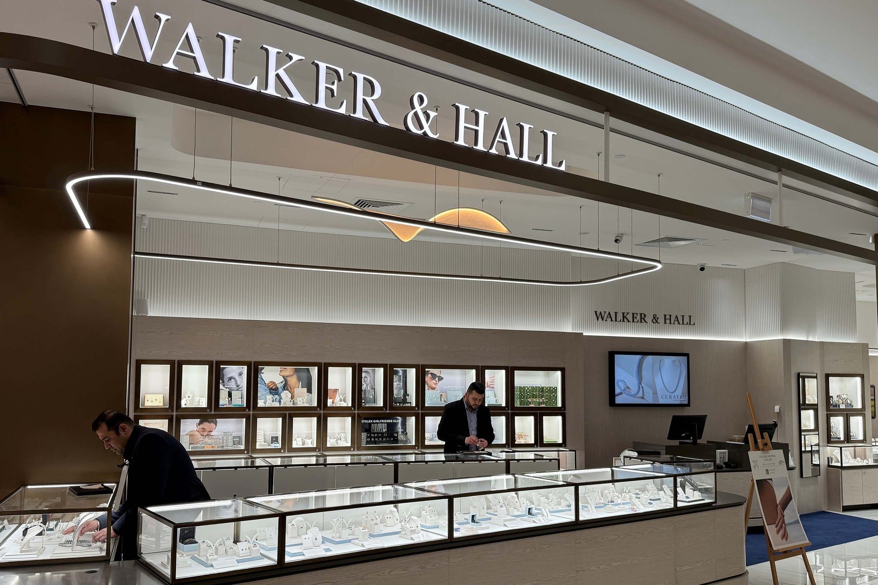 Jewelry store interior with 'Walker & Hall' sign and customers browsing.