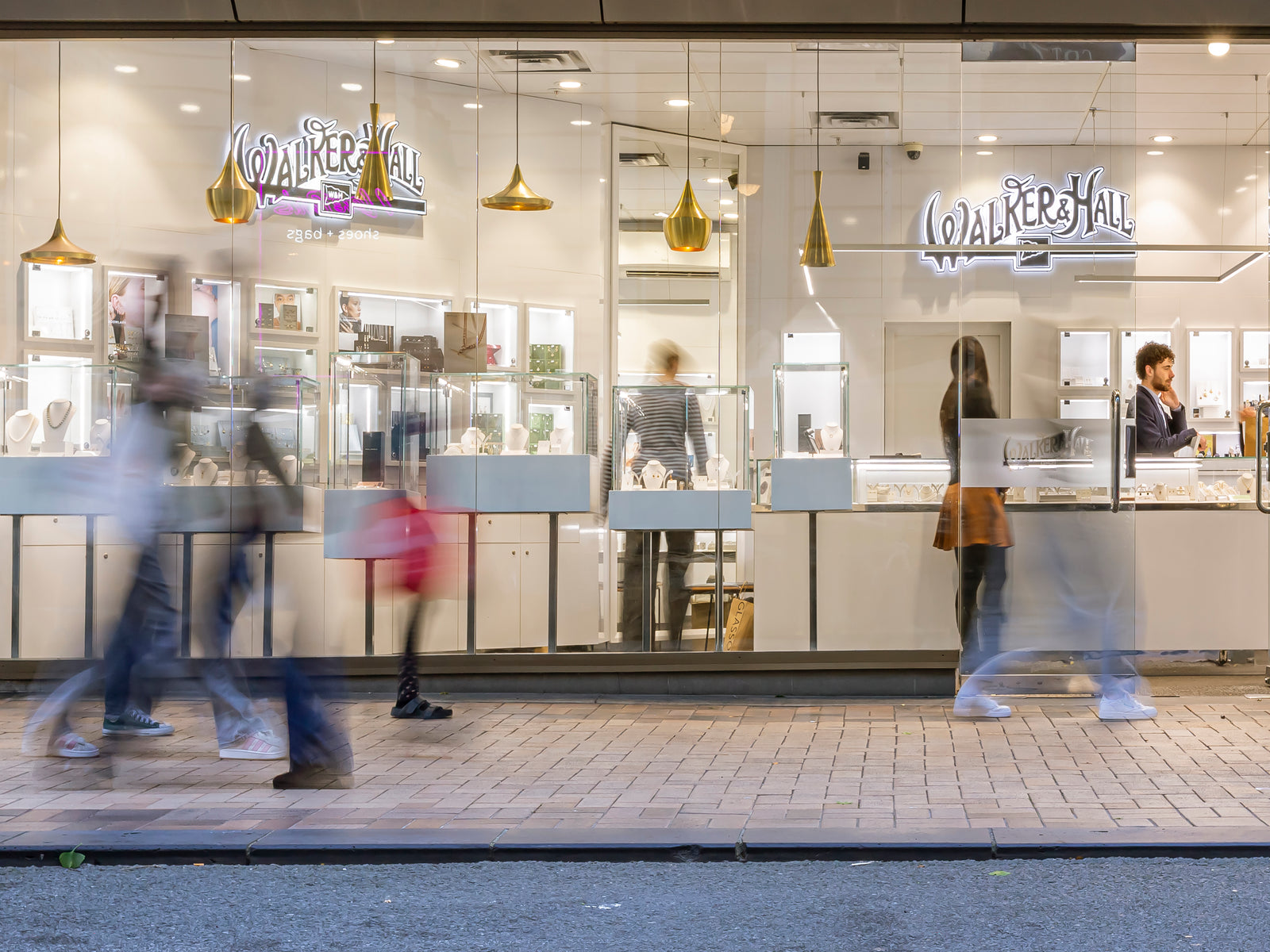 Glass storefront with 'Walker Hall' branding, people walking by on a sidewalk.