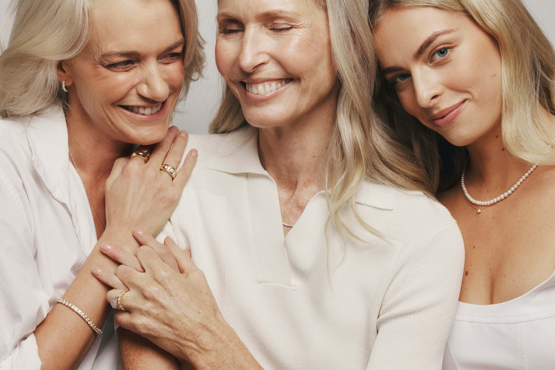 Mother, daughter and granddaughter sitting together holding hands. Wearing natural diamond and pearl jewellery