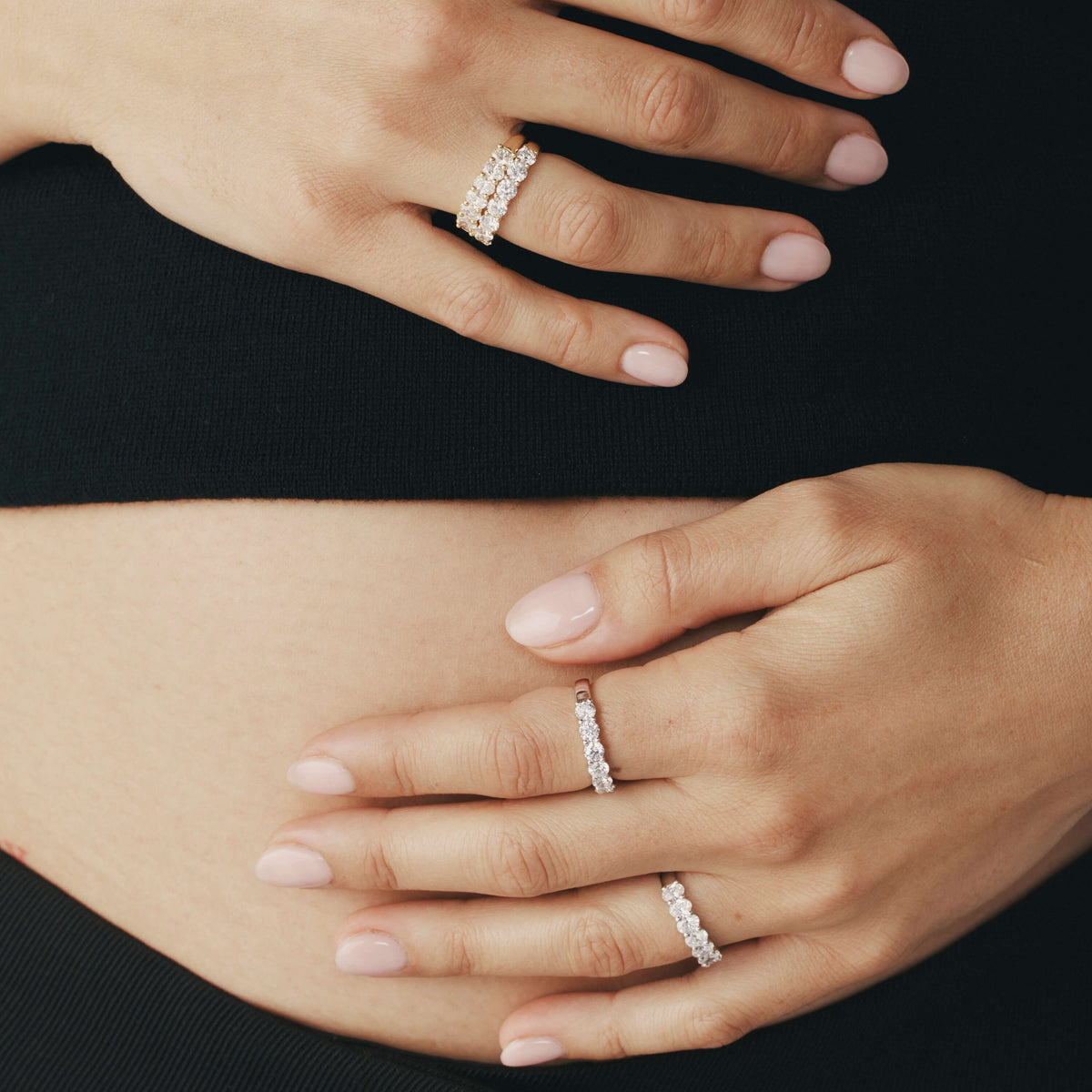 Close-up of hands wearing diamond Panorama rings resting on a pregnant stomach