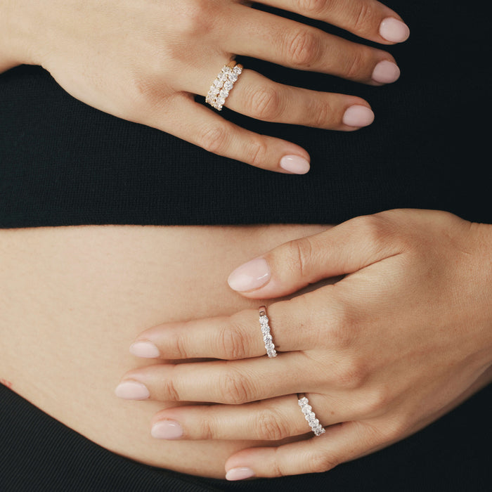 Close-up of hands wearing diamond Panorama rings resting on a pregnant stomach