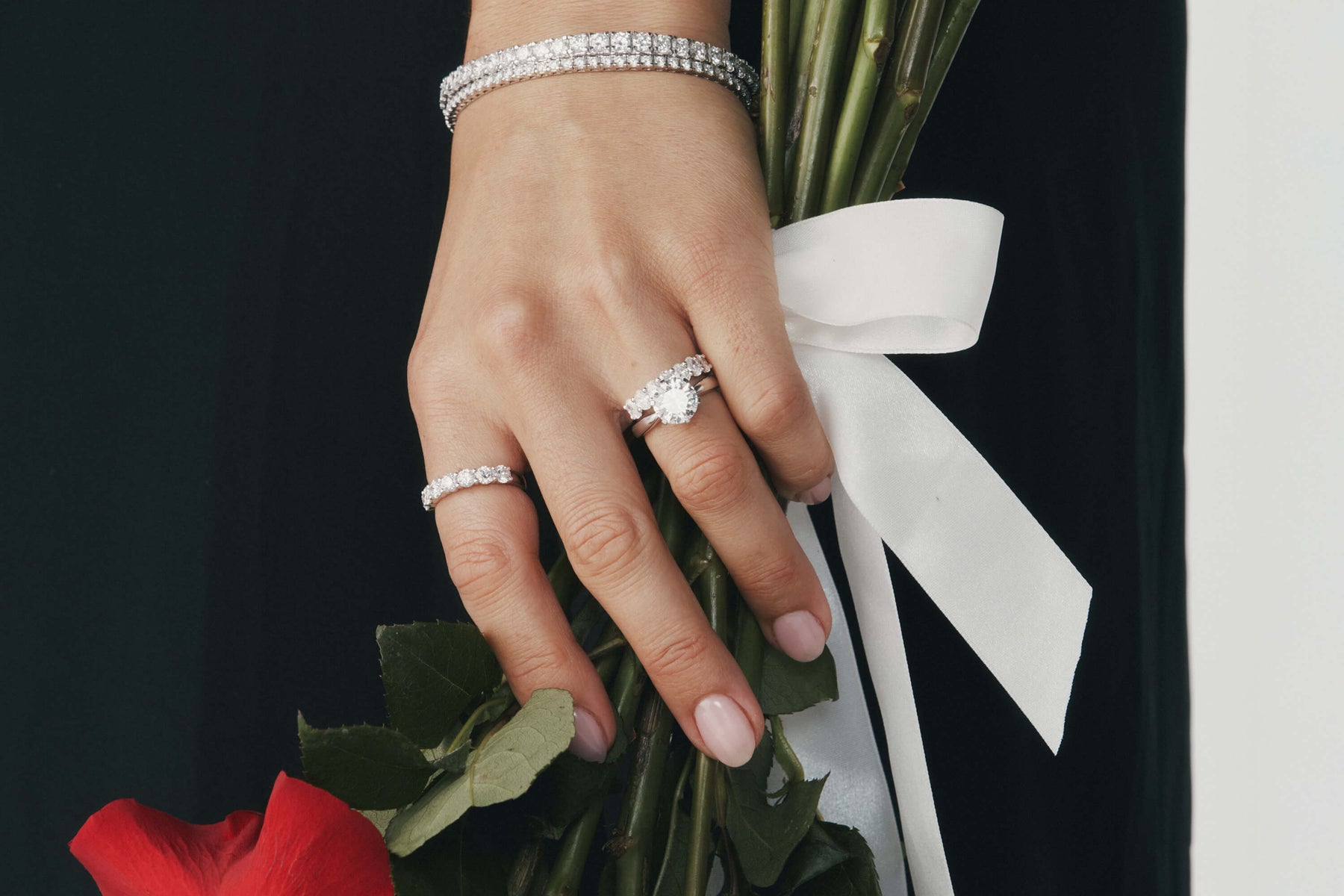 Hand wearing diamond engagement and wedding rings holding a bouquet of red roses