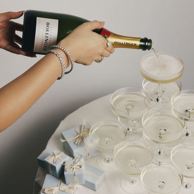 Person pouring champagne from a Bollinger bottle into glasses on a table with Walker & Hall gift boxes.