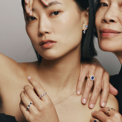 Two women wearing sapphire and diamond jewellery, including rings and earrings, against a neutral background.