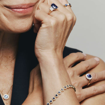 Close-up of a person wearing multiple sapphire rings on a neutral background