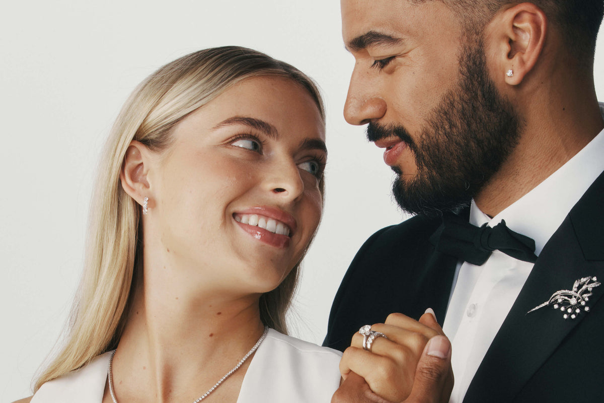 Couple holding hands and looking at one another wearing diamond jewellery