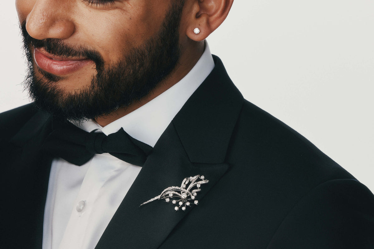 Man wearing a black tuxedo with a bow tie wearing a Vintage diamond brooch and diamond stud earring