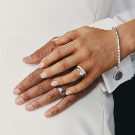 Close-up of two hands wearing diamond engagement and wedding rings on a white background