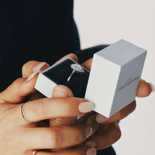 Model holding a Walker & Hall ring box with a natural diamond engagement ring inside