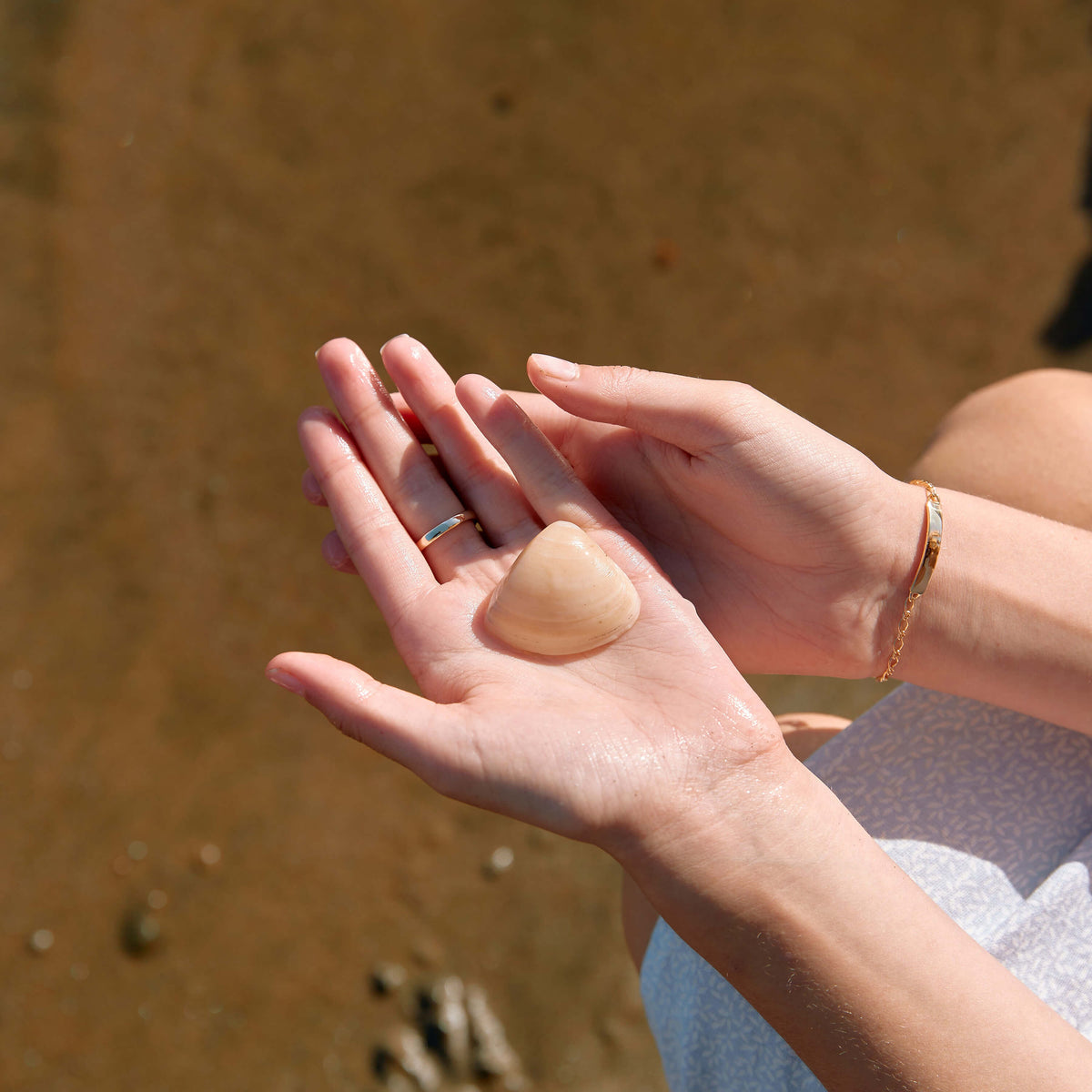 Model holding shell in her hand with NZ beach in the background